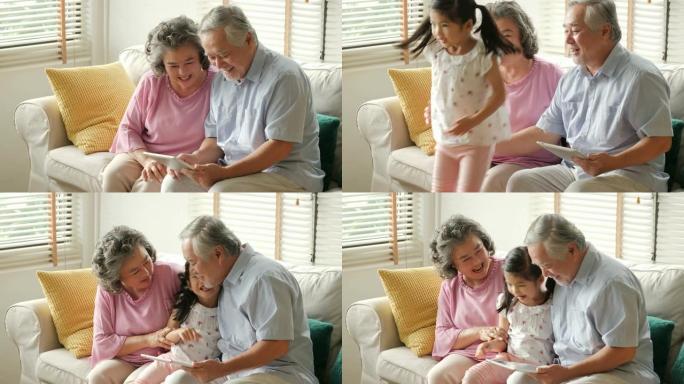 小女孩在玩平板电脑时拥抱她的祖父和祖父。孩子带着快乐的情感和高级男女一起玩。有家庭、生活方式、科技观