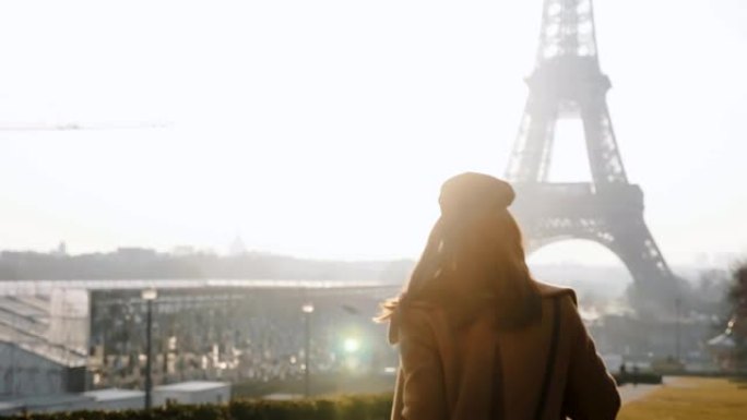 相机跟随快乐的当地博主女人散步，在雄伟的巴黎埃菲尔铁塔附近摆姿势，对着相机慢动作微笑。