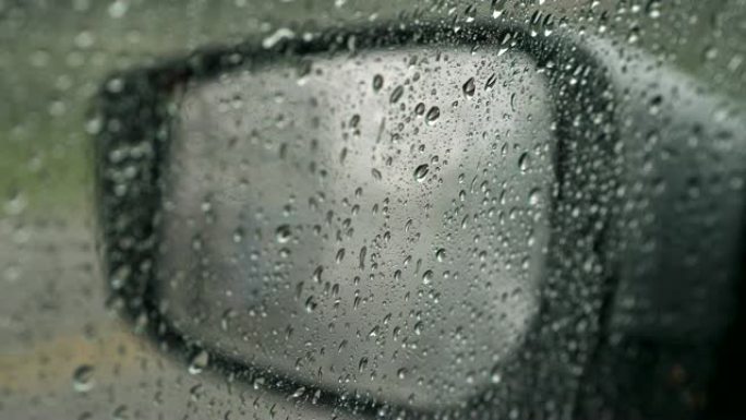 下雨时车窗和镜子上的雨滴。镜子上的散焦交通灯