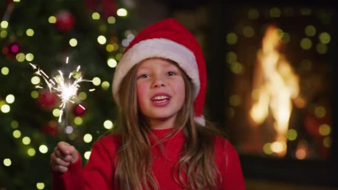 戴着圣诞老人帽子的可爱开朗小女孩的慢动作，手里拿着烟火唱着圣诞歌曲。
