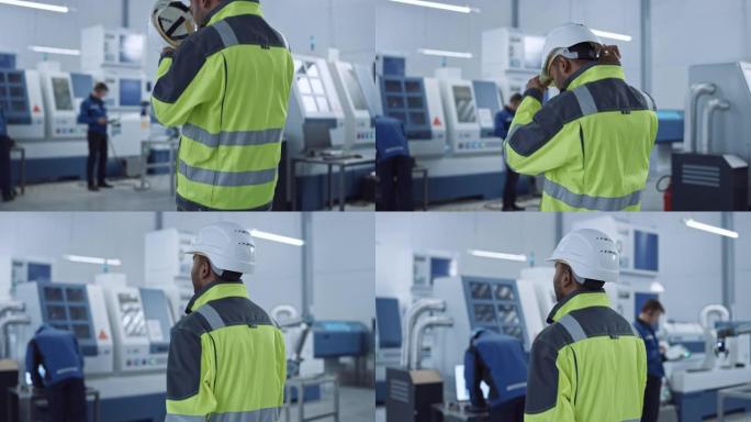 工业4工厂: 现代工人穿着安全夹克戴上安全帽，走过当代工业车间，专业人员在那里工作和编程数控机械。后