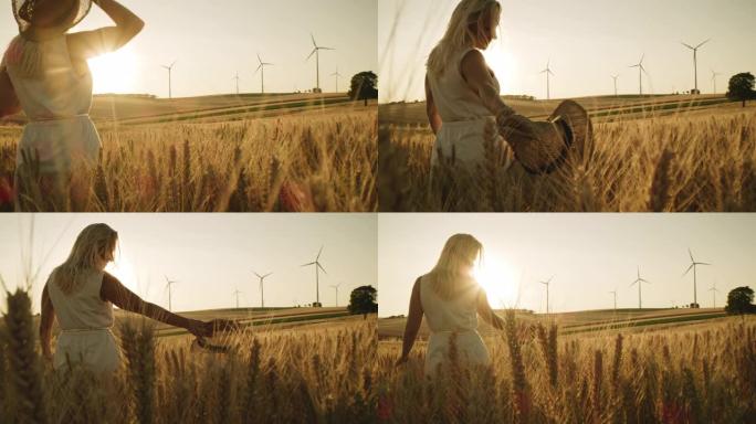 一个女人用她的太阳帽抚摸着小麦植物，同时看着远处的风力涡轮机
