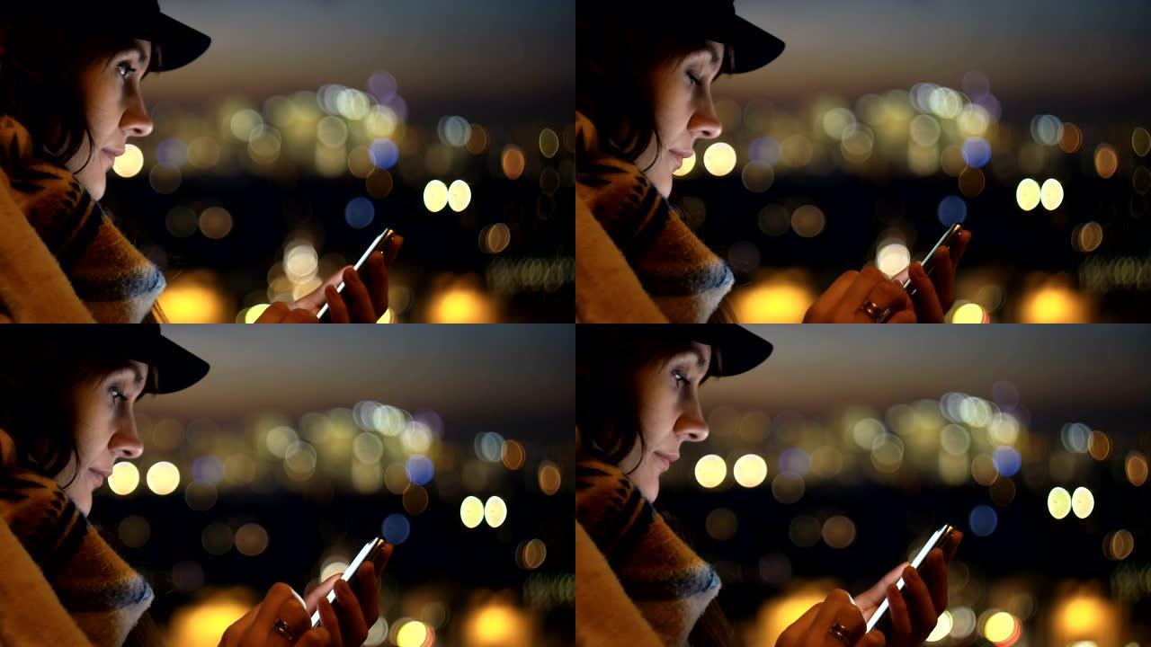特写快乐美丽的女人在模糊的夜城背景下使用智能手机，她的脸被屏幕慢动作照亮。