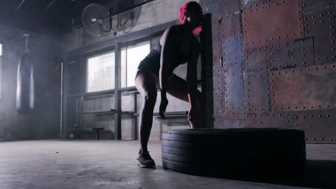 强壮的女人在推轮胎。女人用大轮胎锻炼。在健身房刻苦训练。武术