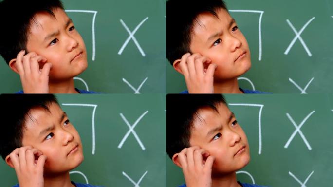 有思想的亚洲小学生在教室4k上挠头在黑板上的前视图