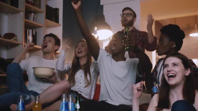 快乐微笑的多民族年轻朋友一起观看足球比赛，庆祝球队胜利并在屏幕上大喊大叫。