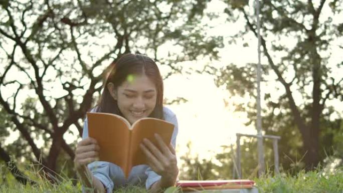日落时，年轻迷人的亚洲女性在公园的绿草地上躺着看书的慢动作镜头。