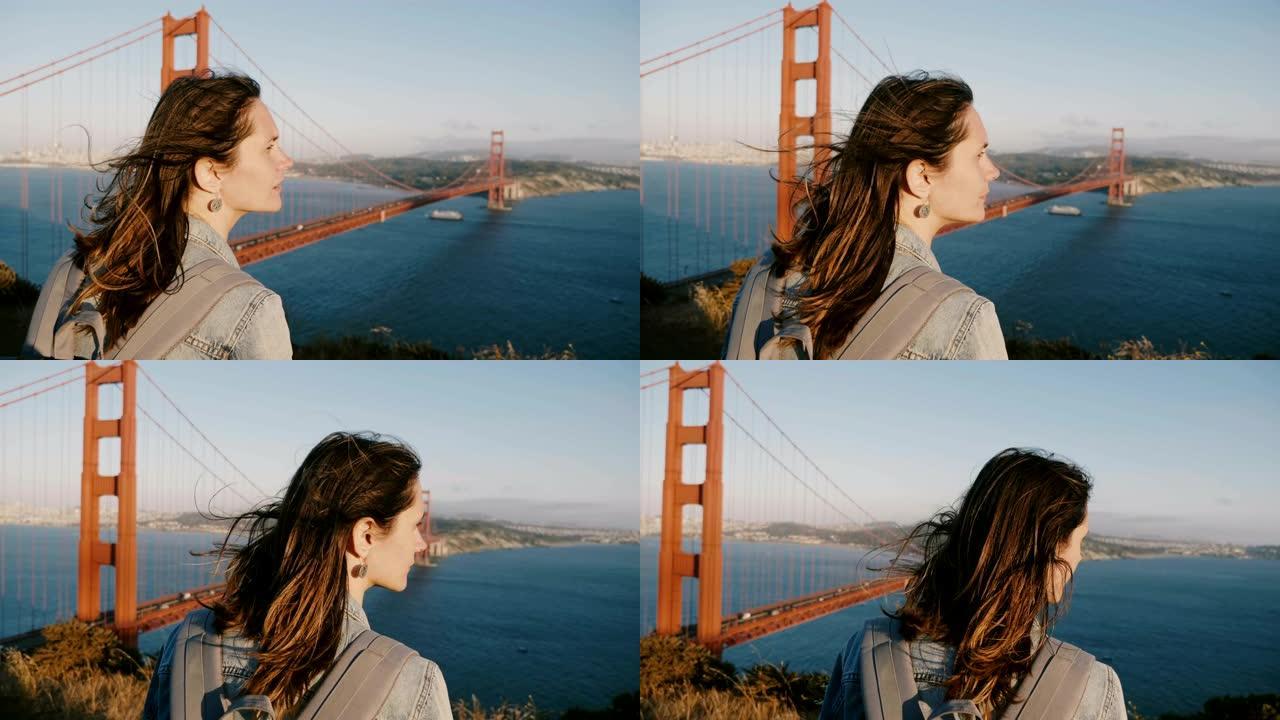 宁静的年轻旅游女子，头发在强风中吹动，在标志性的金门大桥享受史诗般的日落全景