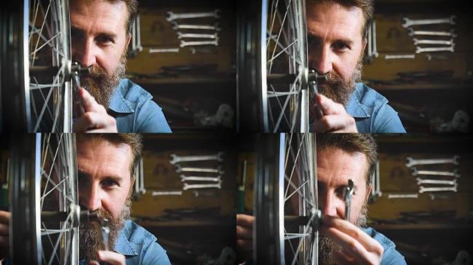 穿着整齐的英俊大胡子的时髦大师，自行车专家，在他的车间修理自行车，车轮，框架，辐条，工具的背景。