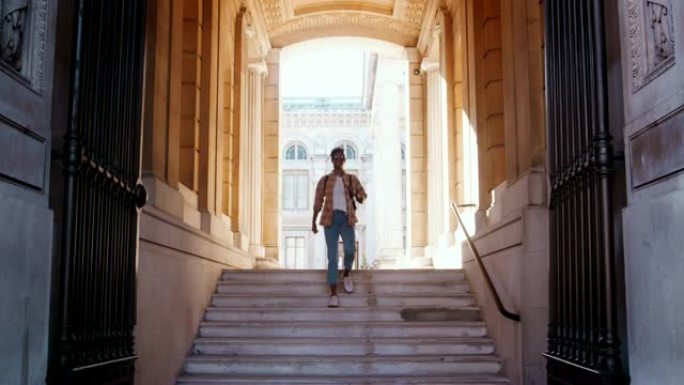一名穿着格子衬衫和蓝色牛仔裤的年轻黑人妇女沿着穿过历史建筑外大门的台阶走下，正面视图
