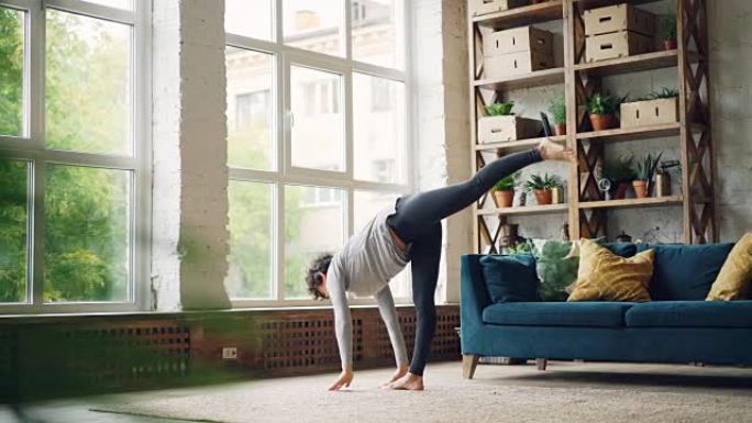 女瑜伽教练正在独自在家练习，练习站在地板上并移动身体的体式。健康活动、自我发展和公寓概念。