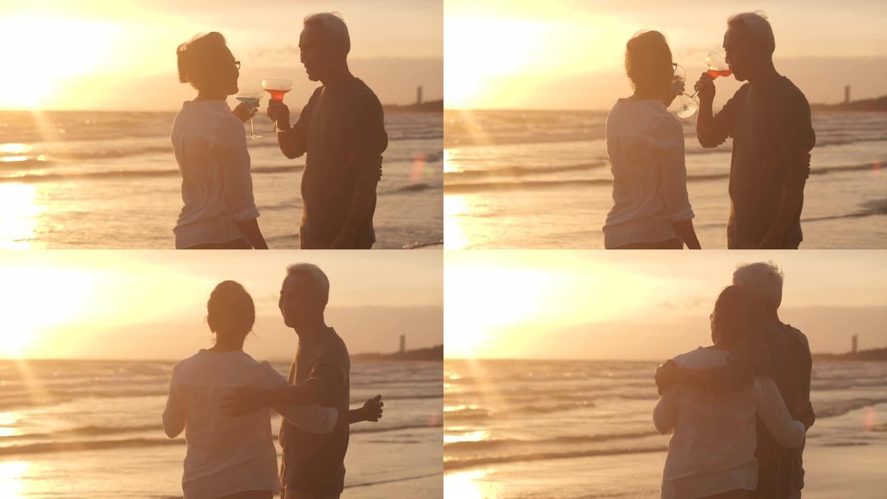 浪漫的亚洲老年夫妇在美丽的热带海滩上慢动作观看日落，享受一杯葡萄酒。