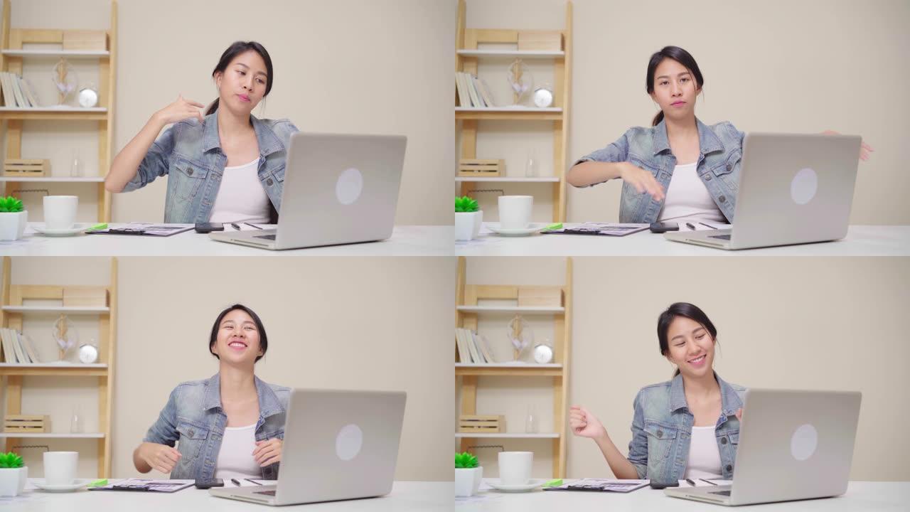 年轻的亚洲妇女在家里的客厅用笔记本电脑工作。亚洲商界女性成功庆典在家庭办公室感觉快乐跳舞。享受在家的