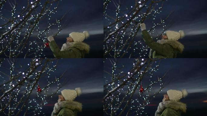 女士在户外树上悬挂圣诞装饰品，并带有串灯