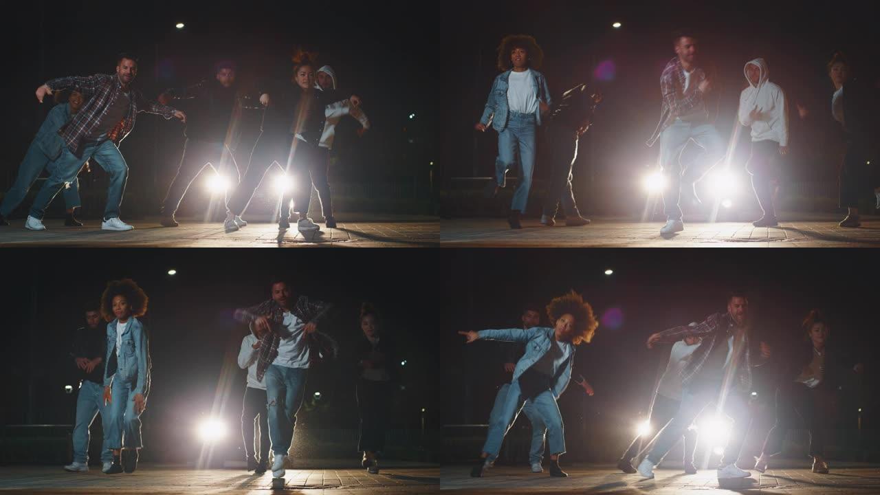 不同种族的年轻城市舞者的慢动作很有趣，晚上在城市停车场用汽车灯训练