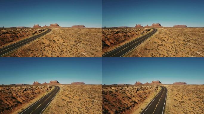 无人驾驶飞机在空的砂岩沙漠公路上左转，在亚利桑那州的纪念碑谷，有着史诗般的平坦山脉。