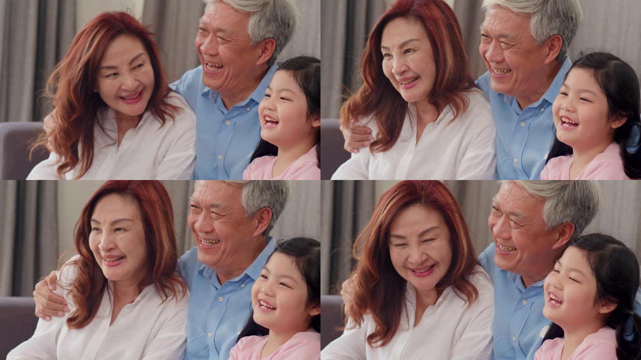 亚洲祖父母在家和孙女聊天。中国老年人，老一代，祖父和祖母的家庭时间与年轻的女孩孩子在客厅的沙发上放松