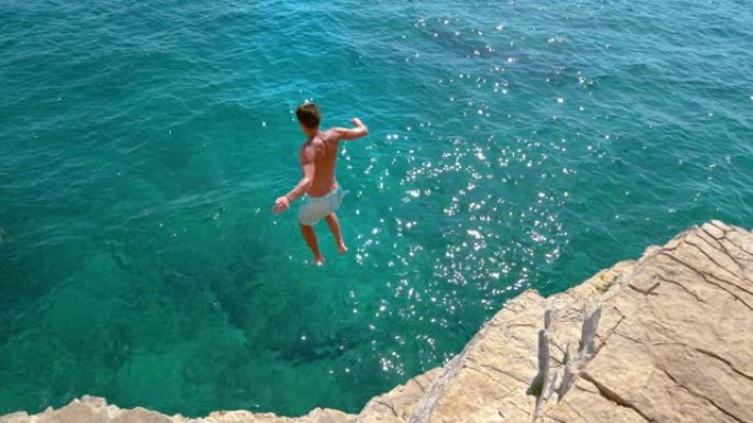 慢动作: 无忧无虑的人从岩石悬崖上潜入深蓝色的大海。