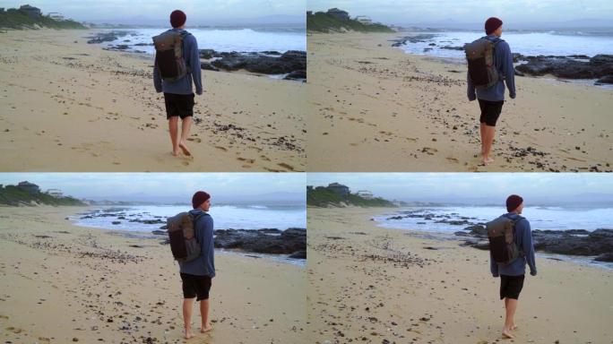 带旅行背包的男孩在海滩上散步
