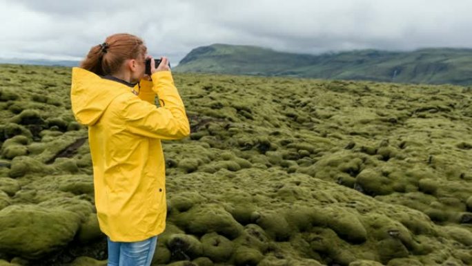 在大风天，女人在冰岛用苔藓覆盖的熔岩田的相机拍照