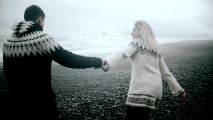 在冰岛的黑海滩岸边散步的年轻夫妇。男人和女人在海岸里奔跑，一起玩乐。