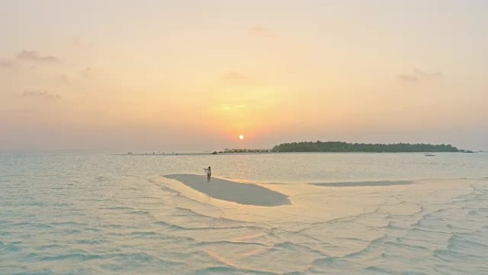 WS无忧无虑的女人在马尔代夫日落时被海洋包围的田园诗般的热带海滩上