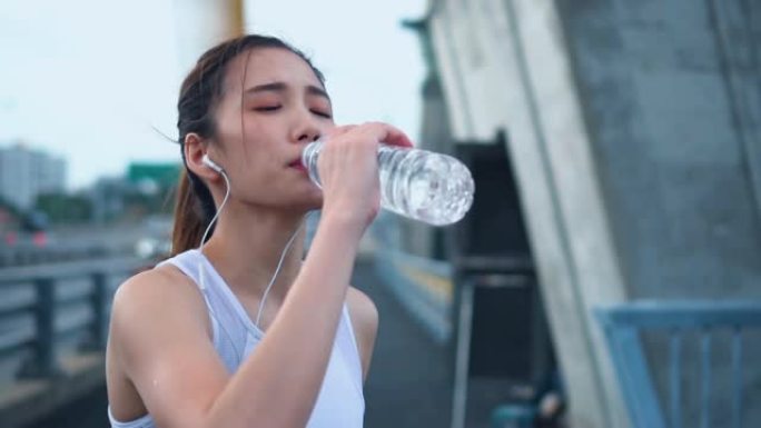 年轻的亚洲运动员女子跑步后喝水，慢动作