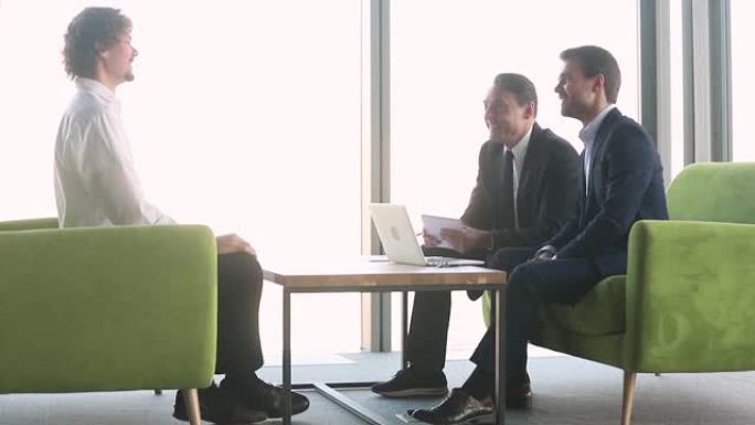 三个积极的商人聚集在一起坐在现代办公室走廊上