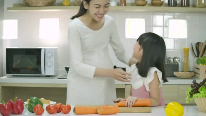 微笑的怀孕母亲和女儿喜欢一起在厨房准备健康的晚餐。母亲教女儿做饭。