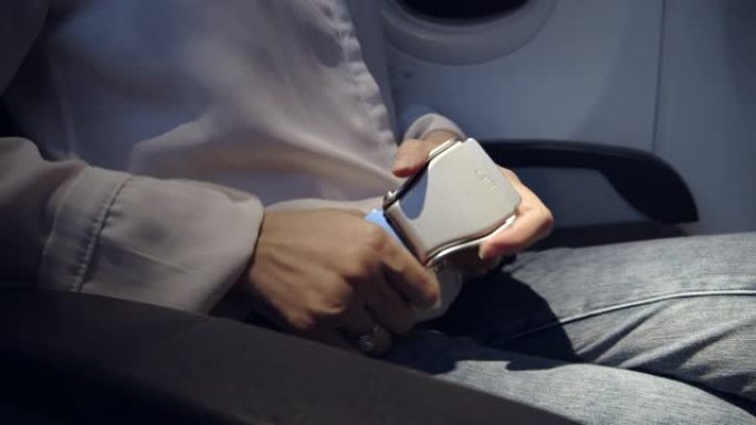 坐在飞机上，穿着白衬衫的亚洲女性乘客系好安全带。