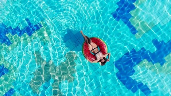 戴帽子的女孩躺在橡皮圈上的游泳池里。