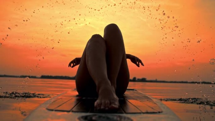 超级慢动作莫女人泼水，而放松在一个冲浪板在日落