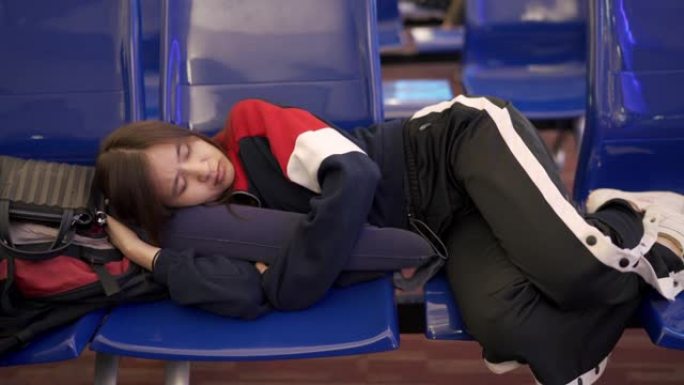 在机场航站楼，运输站和旅客旅行等待航班时，两次射击使亚洲妇女用枕头睡觉