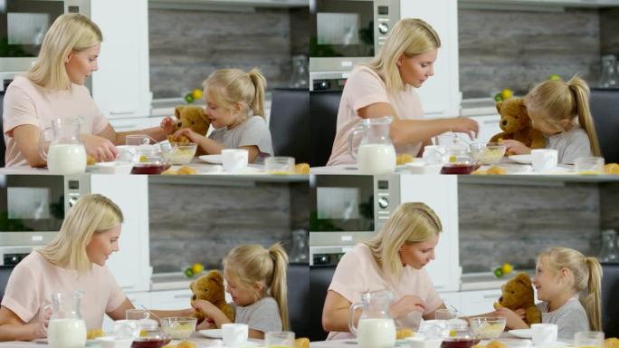 小女孩和妈妈在早餐时喂熊玩具