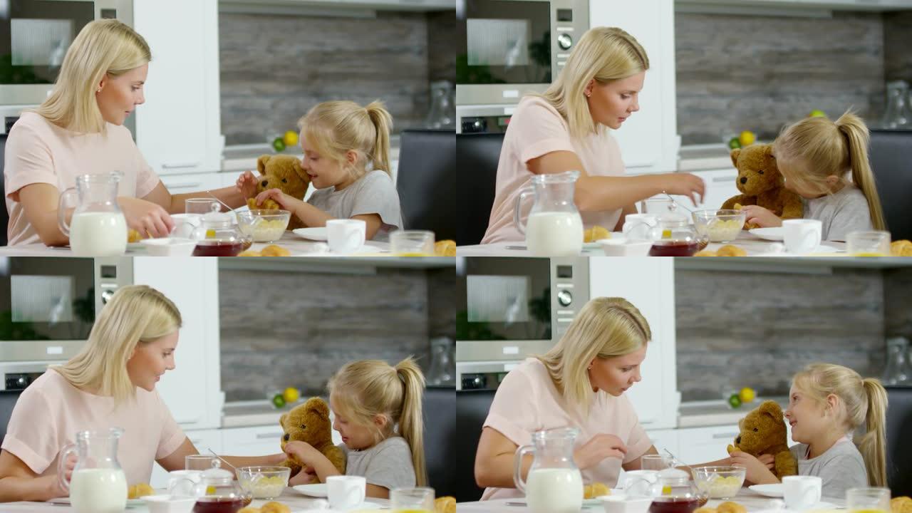 小女孩和妈妈在早餐时喂熊玩具