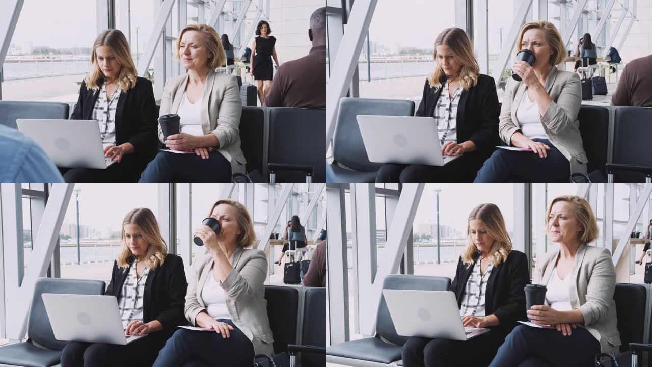 两名女商人在飞行前坐在机场候机室里，用笔记本电脑工作，以慢动作喝咖啡