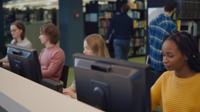 大学图书馆: 多种多样的多民族学生从事计算机工作，学习，考试学习，写论文，研究课堂作业，与同学交谈。