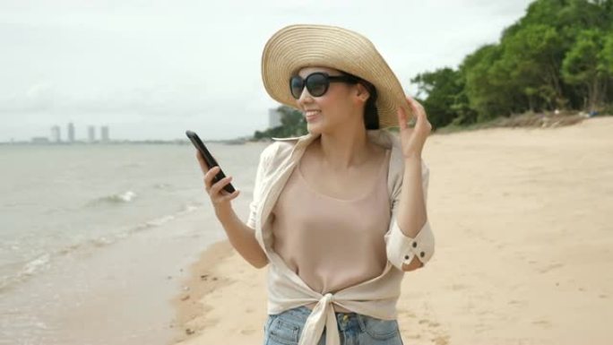 年轻的亚洲妇女在沙滩上走路和使用手机
