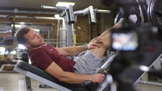 健身教练躺在压腿机上，对着镜头说话