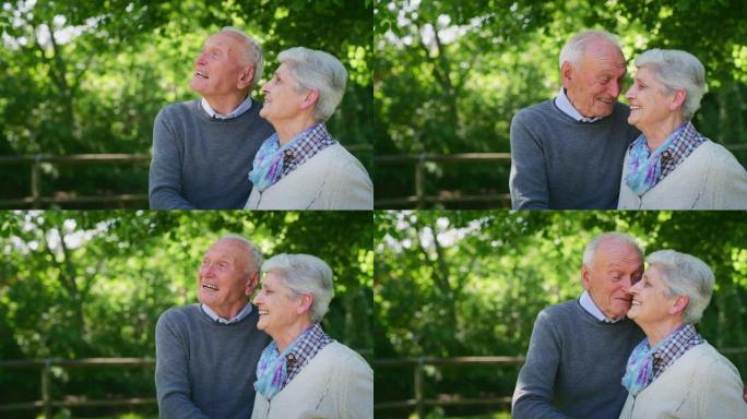 在阳光明媚的日子里，一对幸福的老年夫妇的慢动作拥抱着感情，这是他们在绿色公园里永远相互爱和尊重的标志