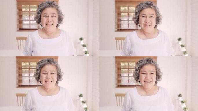 亚洲老年妇女在家里的客厅沙发上放松时，微笑着看着相机，感到快乐。生活方式高级女性在家的概念。