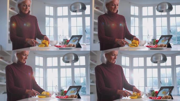 成熟的女人在家里的厨房里遵循数字平板电脑上的食谱