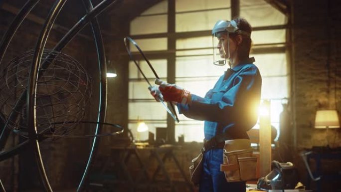 穿着蓝色连身衣和安全面具的年轻当代女艺术家正在工作室的一个管形雕塑上安装一个金属环。赋权女人用钢铁制