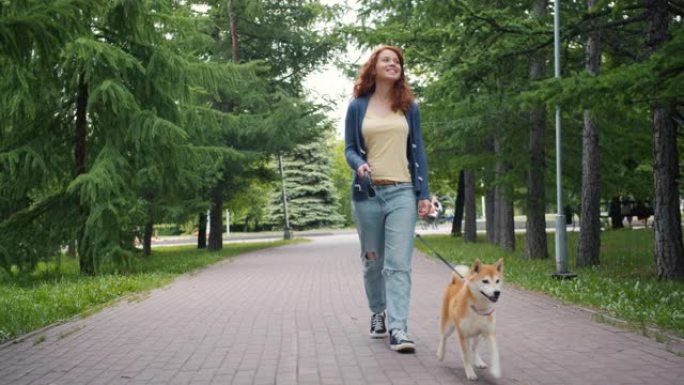 慢动作多莉拍摄美丽的女孩在绿色公园散步良种小狗