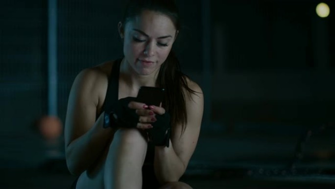 穿着黑色运动服的美丽运动健身女孩在晚上使用智能手机时微笑着。