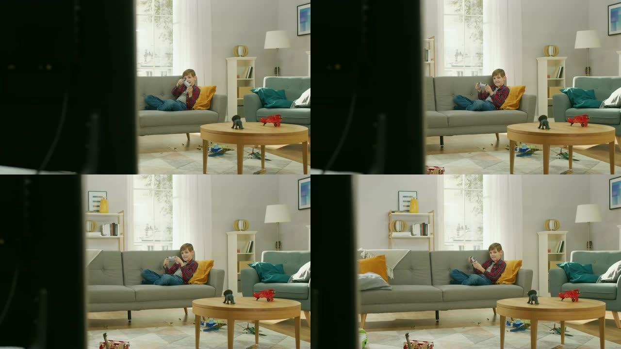可爱的小男孩躺在沙发上，使用操纵杆控制器在电视控制台上玩视频游戏。男孩在家里玩电子游戏。