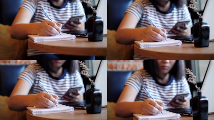 女人用手机在笔记本上工作和写字，在家工作