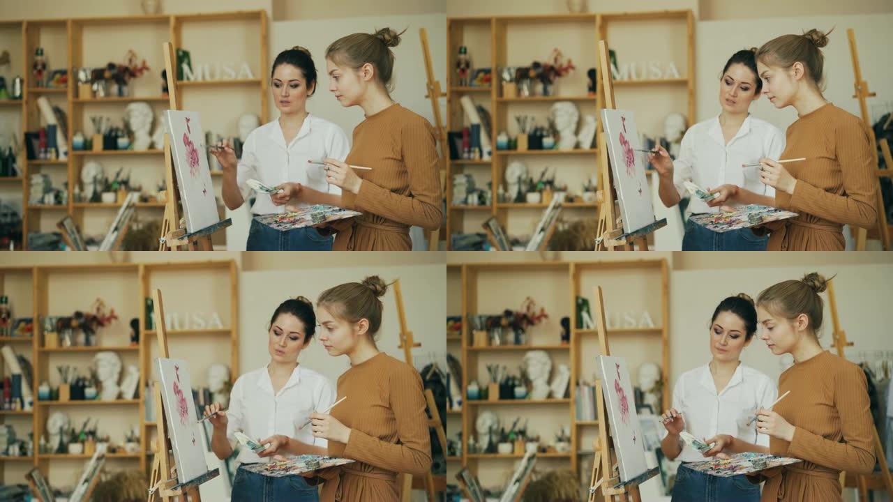 经验丰富的绘画老师正在与她的女学生站在画架旁，讨论艺术品。可以看到带有工具的架子。