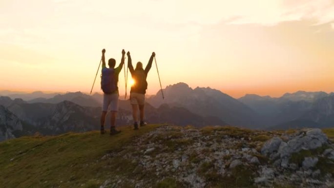 空中: 年轻的徒步旅行者夫妇在捕捉日落时伸出双臂。