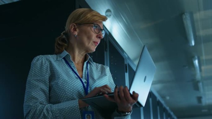 在数据中心: 使用笔记本电脑的专业女性IT专家的肖像，对服务器机架进行维护和诊断。低角度相机拍摄。